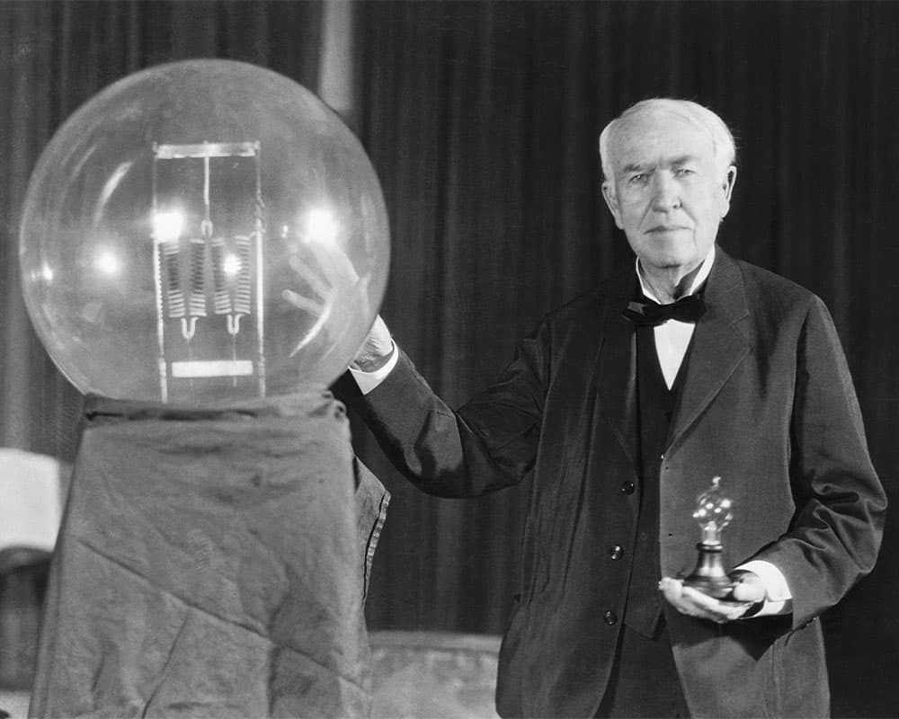 An older Edison with a replica of his first light bulb, as large as a beach ball