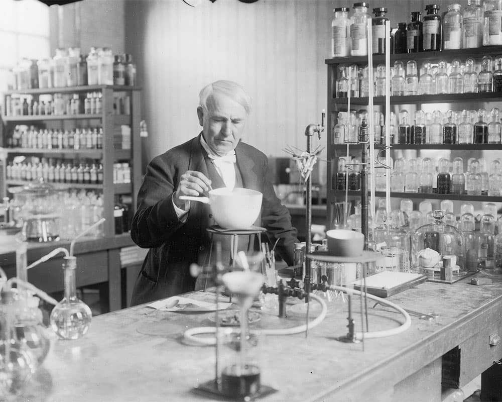 Edison in his laboratory, surrounded by bottles and scientific equipment