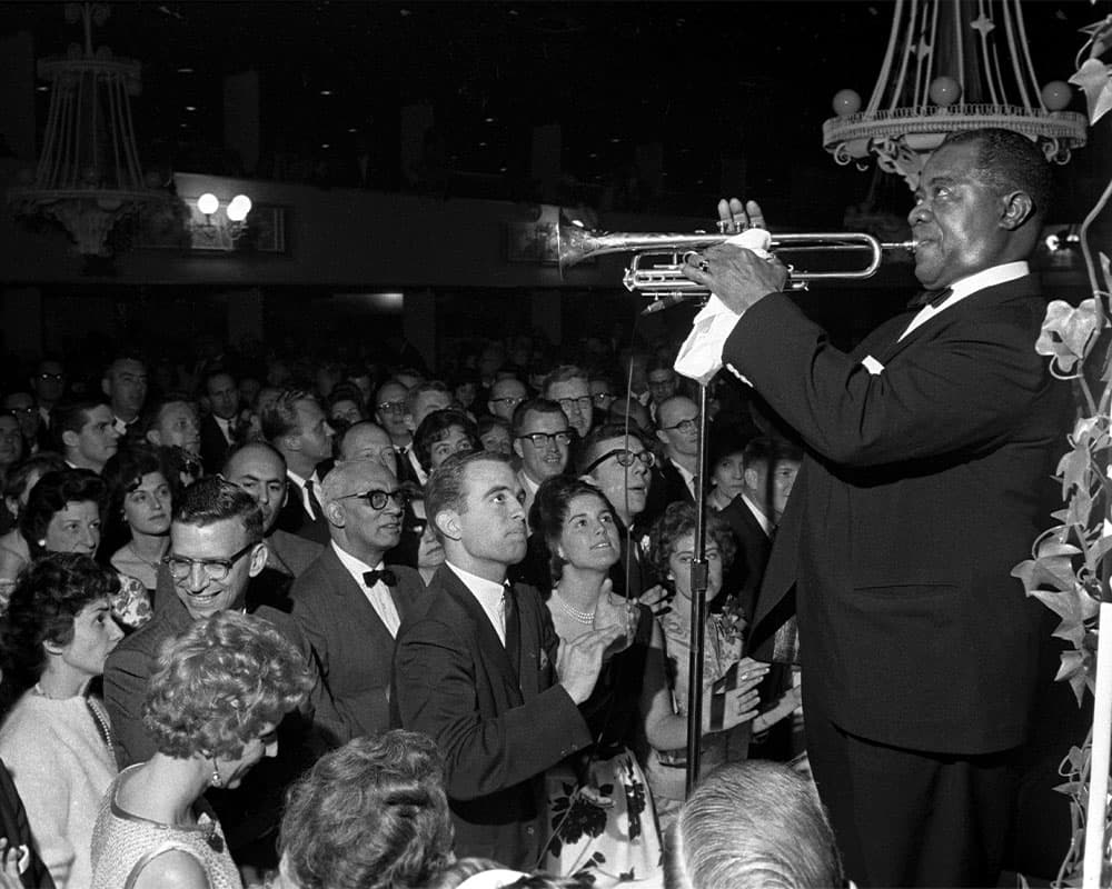 Black & white photo of Armstrong performing in front of a large audience
