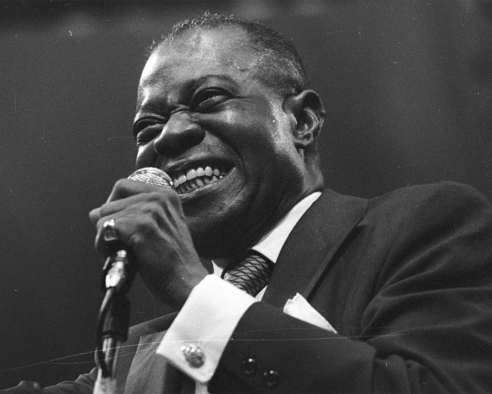 Black & white photo of Armstrong holding a microphone and smiling