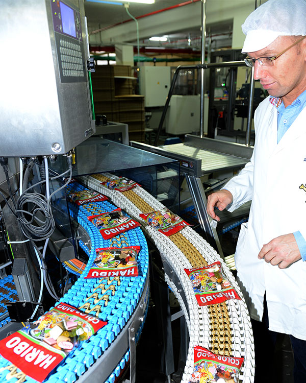 A worker watches over two conveyer belts with snacks on them