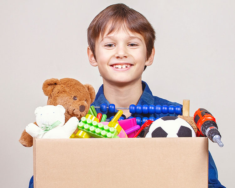 A young boy smiles while carrying a box full of toys.