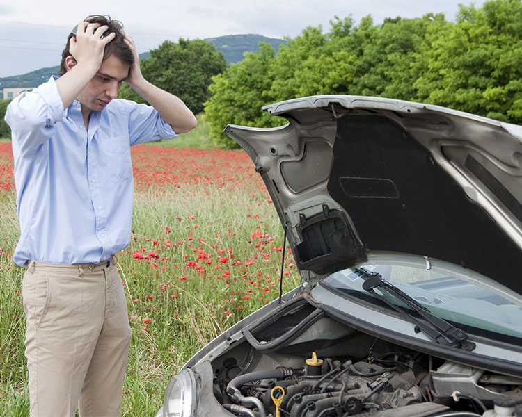 A man holds his hands to his head while looking at his car’s engine