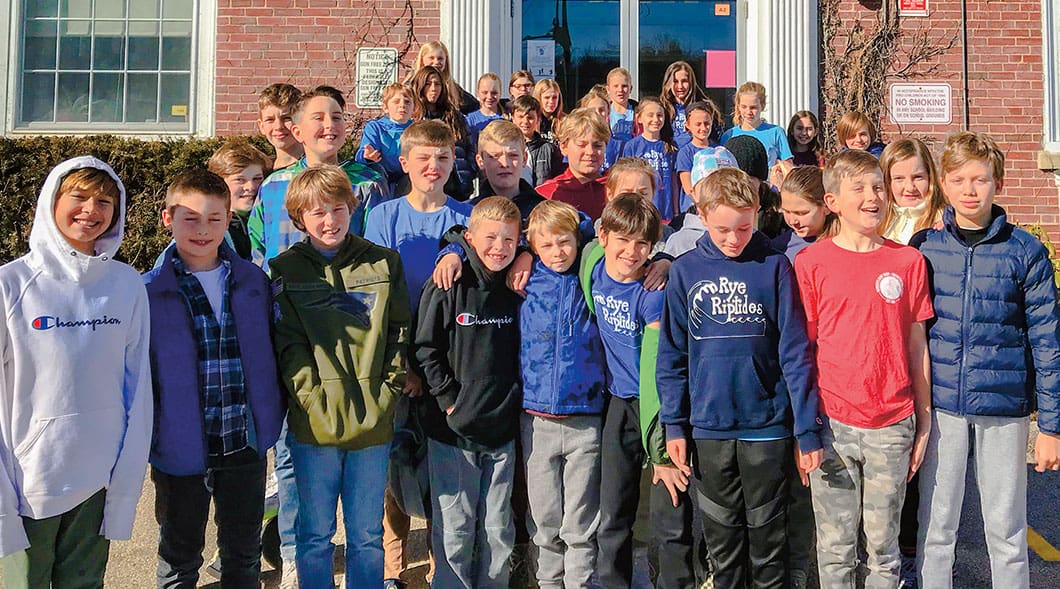 A group of students smile outside their school