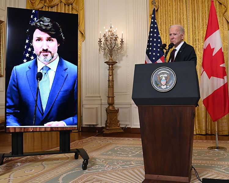 Joe Biden frowns at a podium. Canadian PM Trudeau is on a teleconference screen