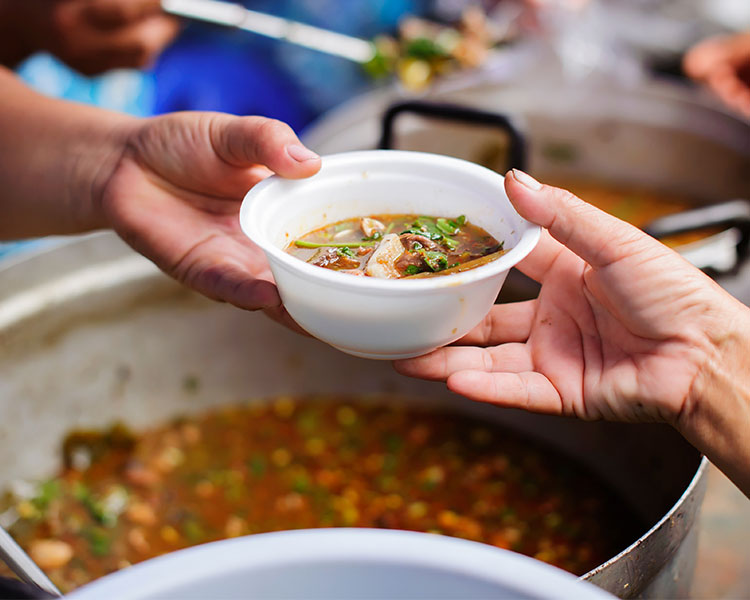 A worker hands a bowl of soup to someone.