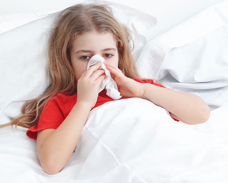 young girl with a cold laying in bed and blowing her nose