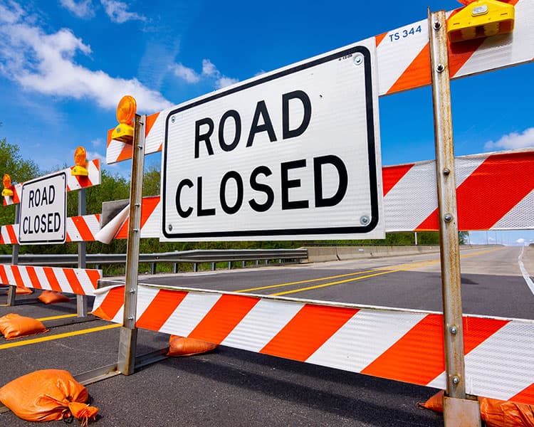 a road blocked off by barriers with a sign saying Road Closed