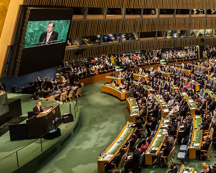 very large auditorium with hundreds of officials watching a man in a suit speak from a podium