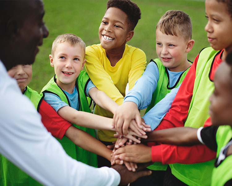 A group of children with their hands on top of each others&apos; as they look to an adult