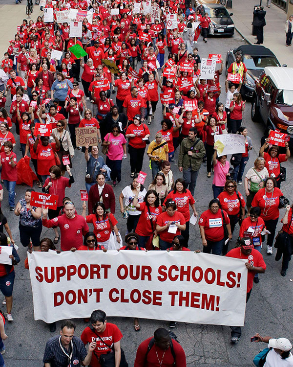 People marching in protest. Banner reads: Support Our Schools! Don&apos;t Close Them!