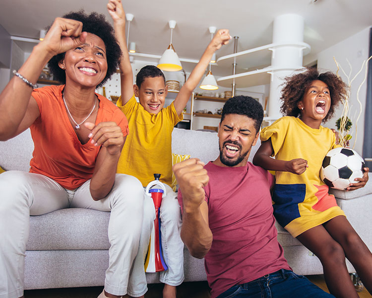 Photo of a family celebrating while sitting on couch and daughter holds soccer ball