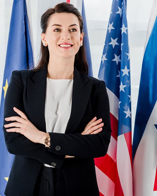 Person wearing a suit while crossing their arms and standing in front of flags