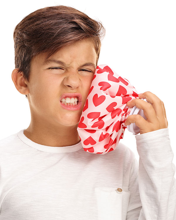 Kid wearing an expression of discomfort and pressing an ice bag to their face