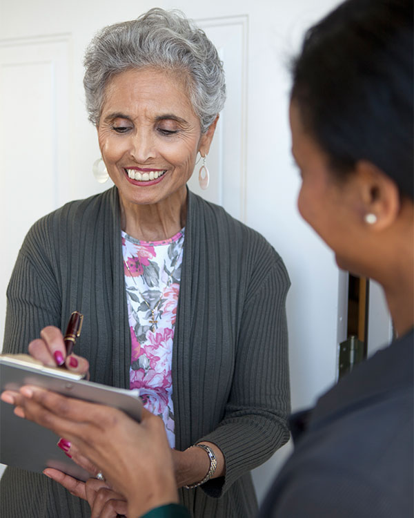 Photo of a smiling person signing a clipboard that another person is holding