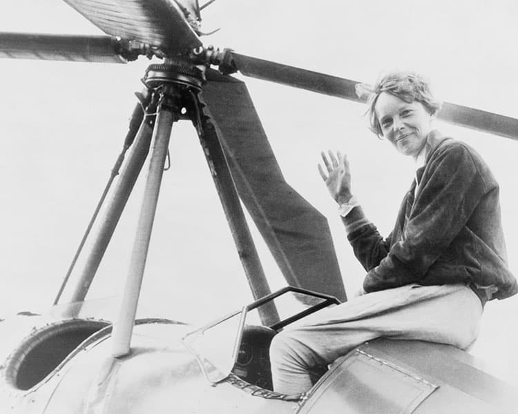 Black & white photo of Amelia Earhart waving from the top of an airplane