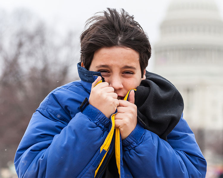 Photo of a kid bringing his jacket up to shield face from cold