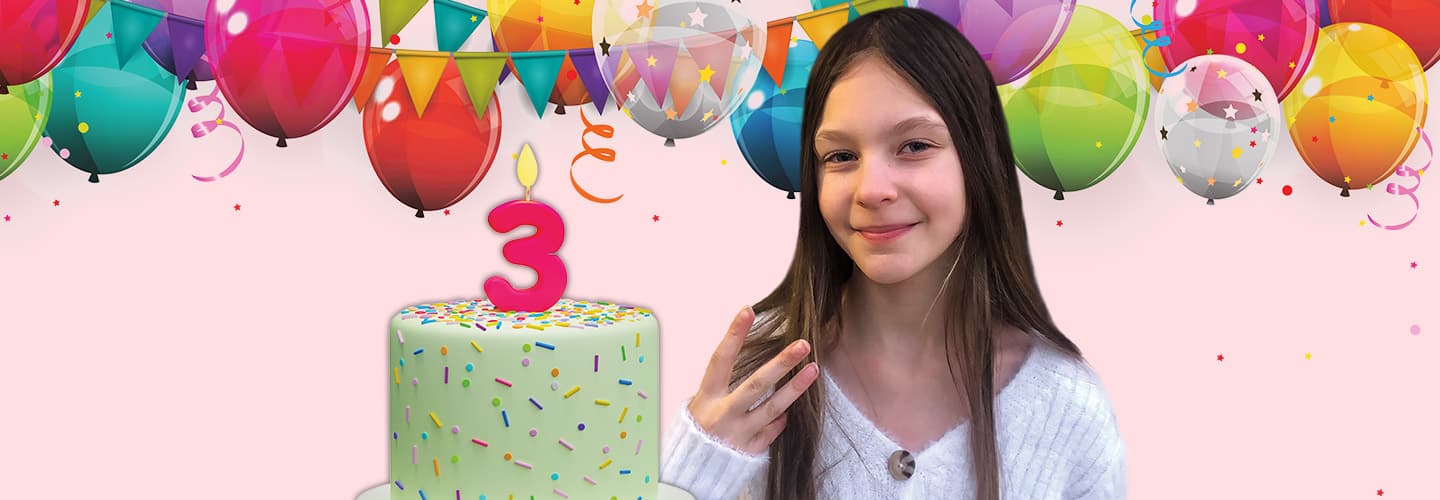 Image of a person holding up three fingers while standing next to cake decorate by a number 3