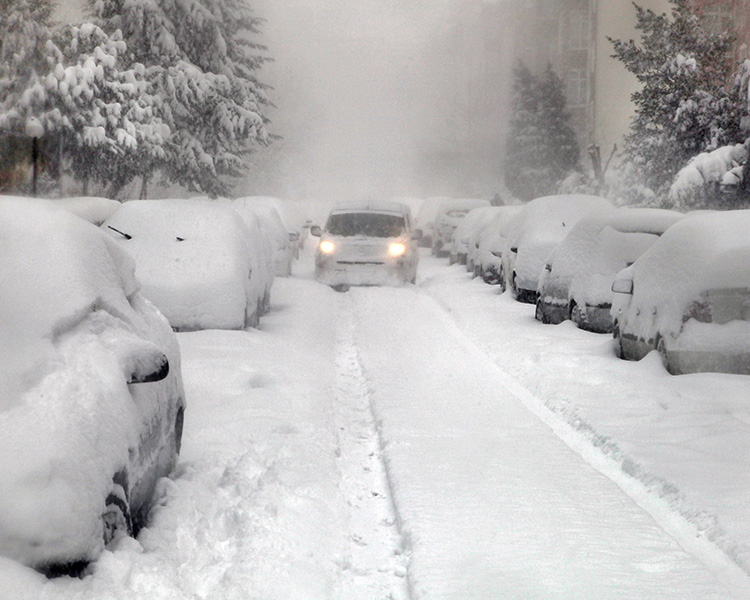 Image of a very snowy city street filled with cars covered in snow