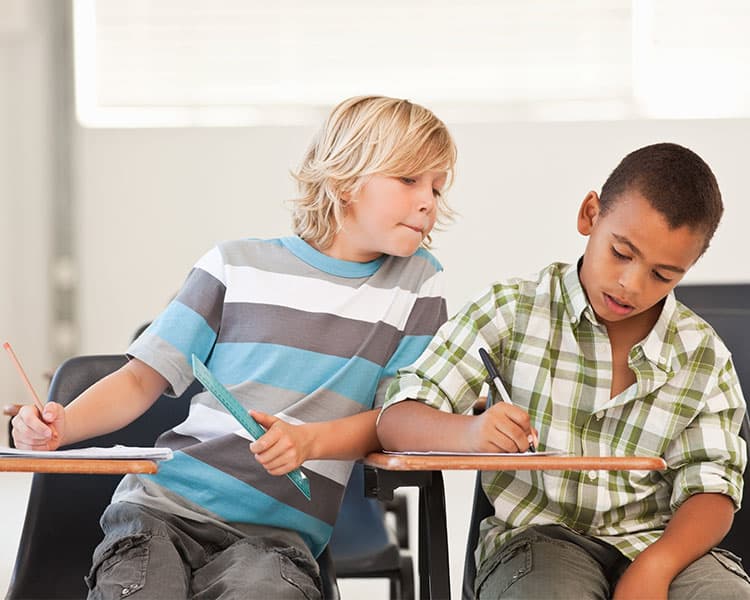 Photo of two students taking a test & one of them looking at the others to copy answers