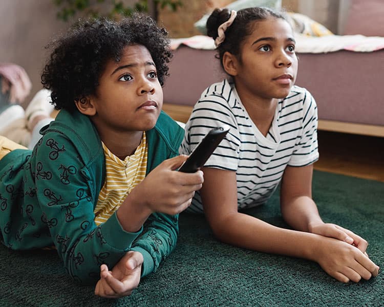 Image of two kids watching television and one holding the remote